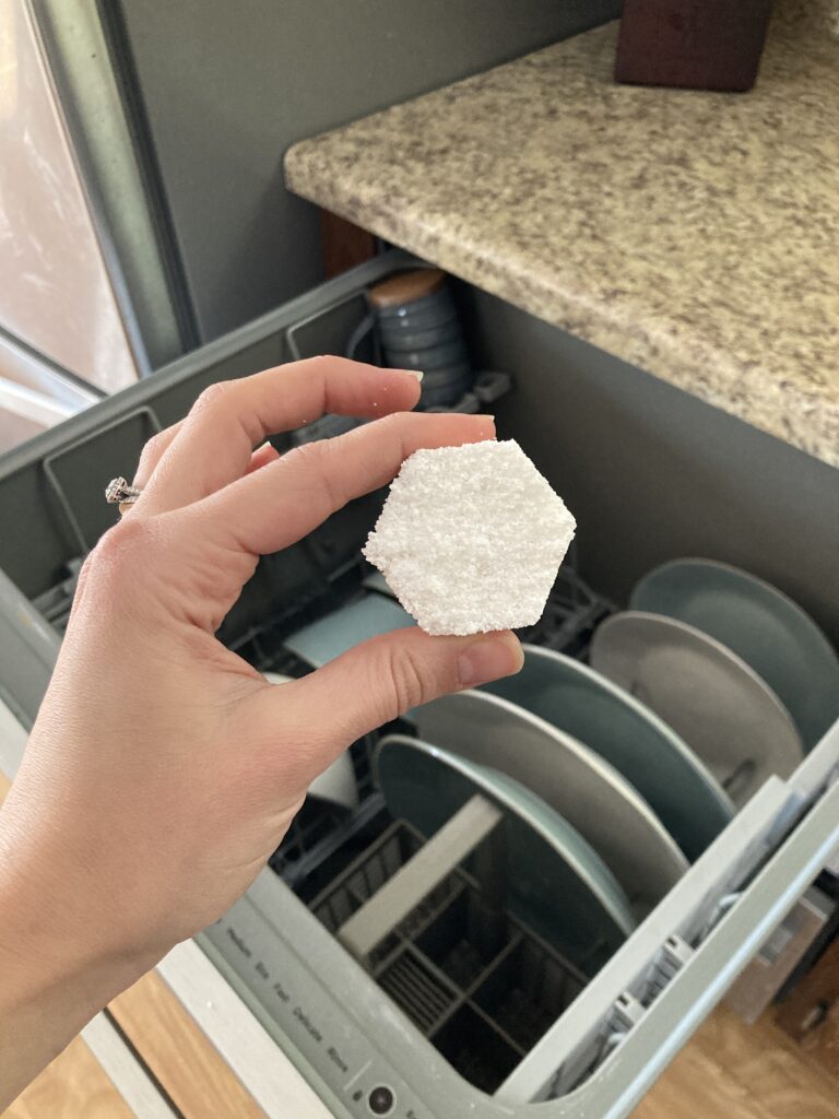 Hand holding up dishwasher pod in front of dishwasher