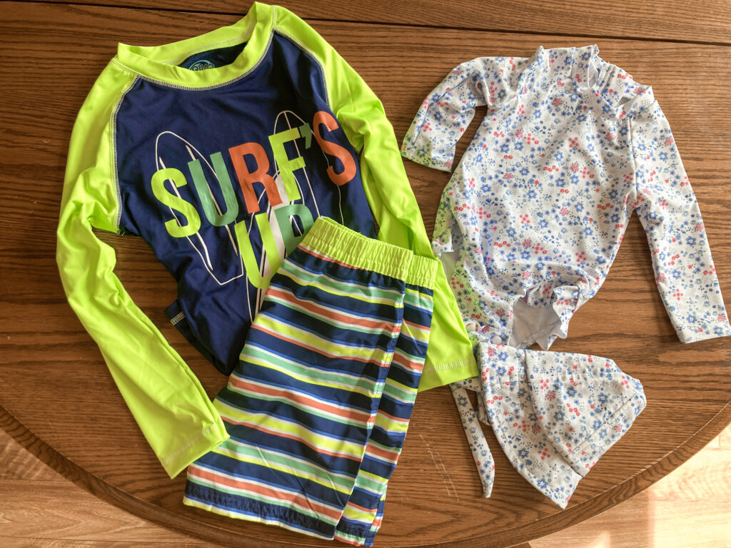 A boys swimsuit and a baby girl swimsuit laying on table