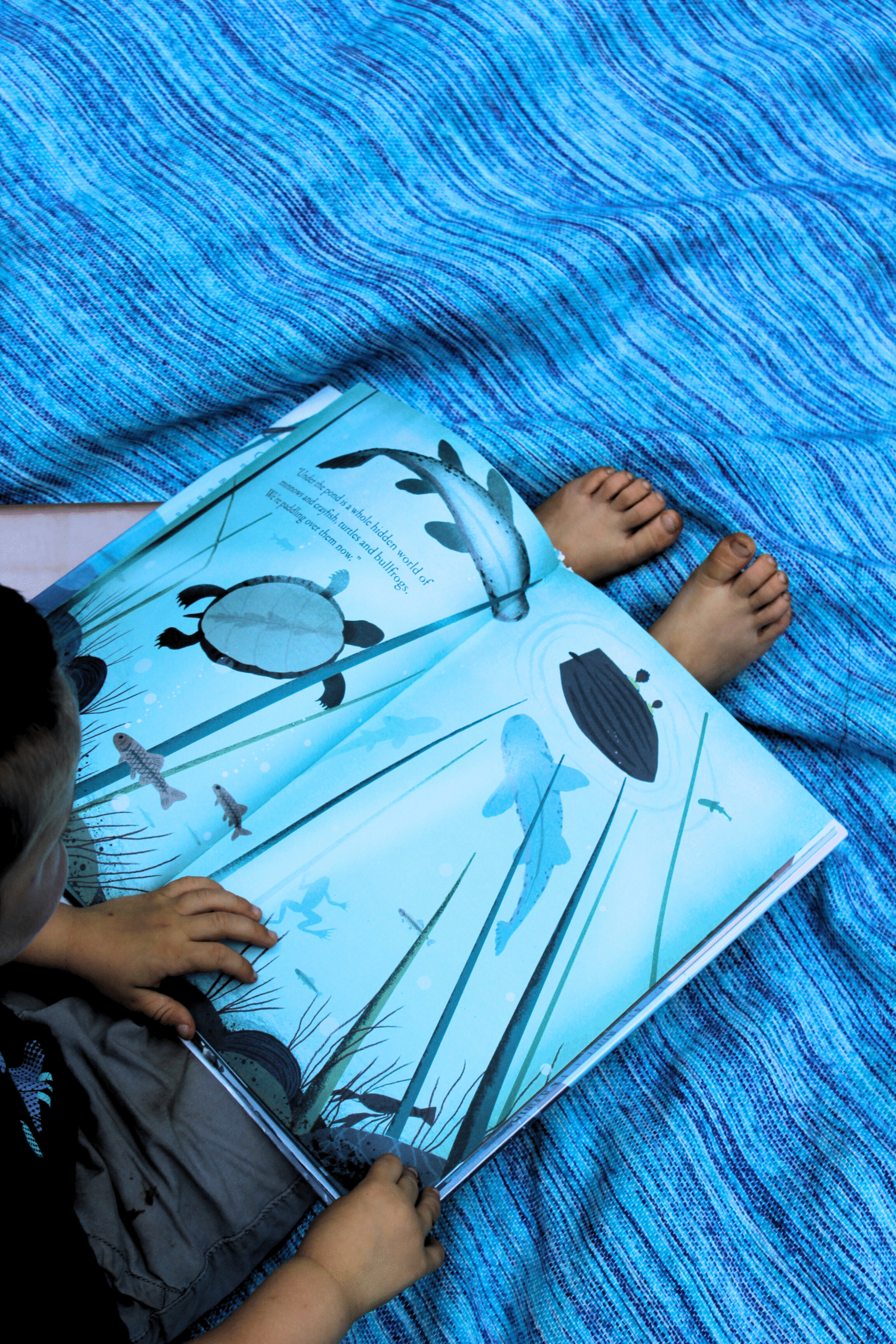 Small boy reading book on a blanket with his toes peeking out