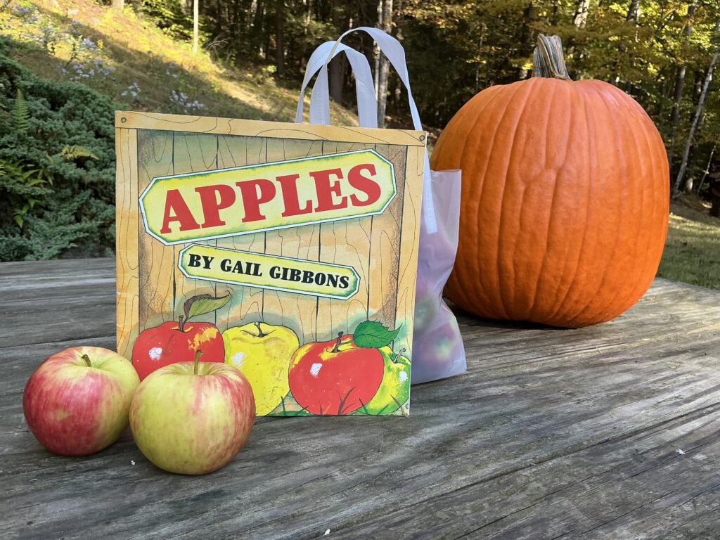 Apples book by Gail Gibbons is propped in front of a pumpkin and some apples in a bag