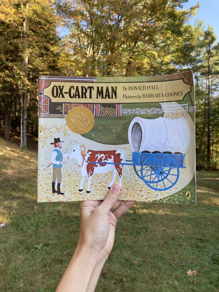 Person holding up the book ox-cart man with trees in the background