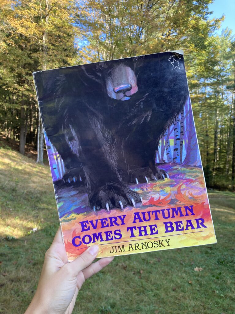 Person holding up the book Every Autumn Comes the Bear with trees in the background