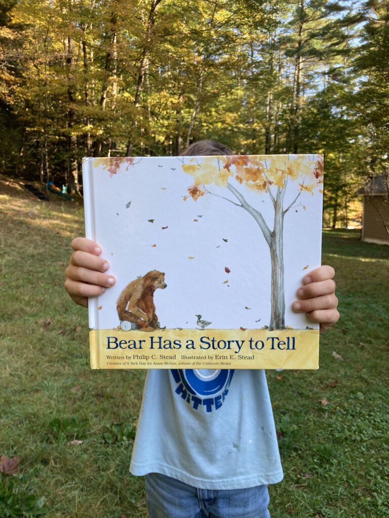 Boy holding a book in front of his face titled Bear Has a Story To Tell