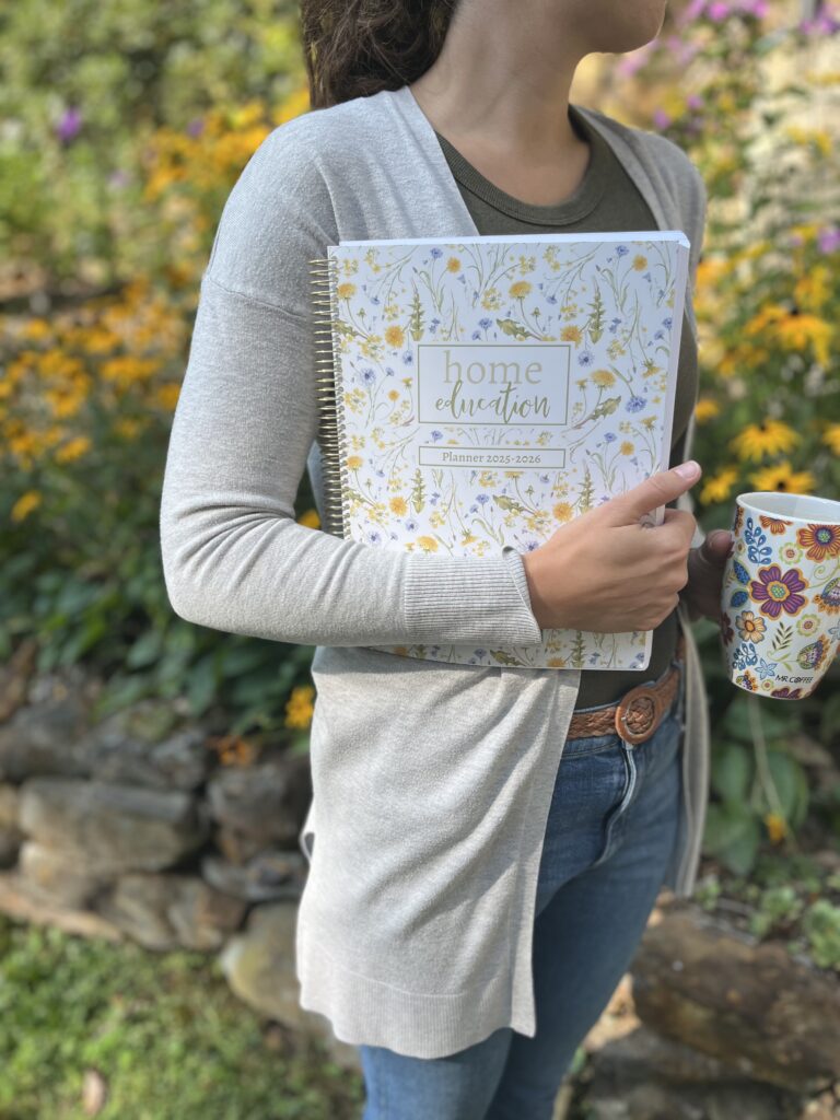 Woman standing outside holding a coffee mug and a lesson planning book