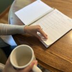 Woman flipping through a planner while she sips her morning coffee