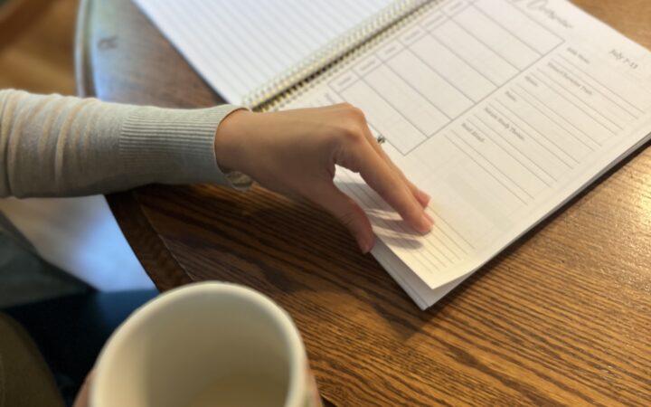 Woman flipping through a planner while she sips her morning coffee