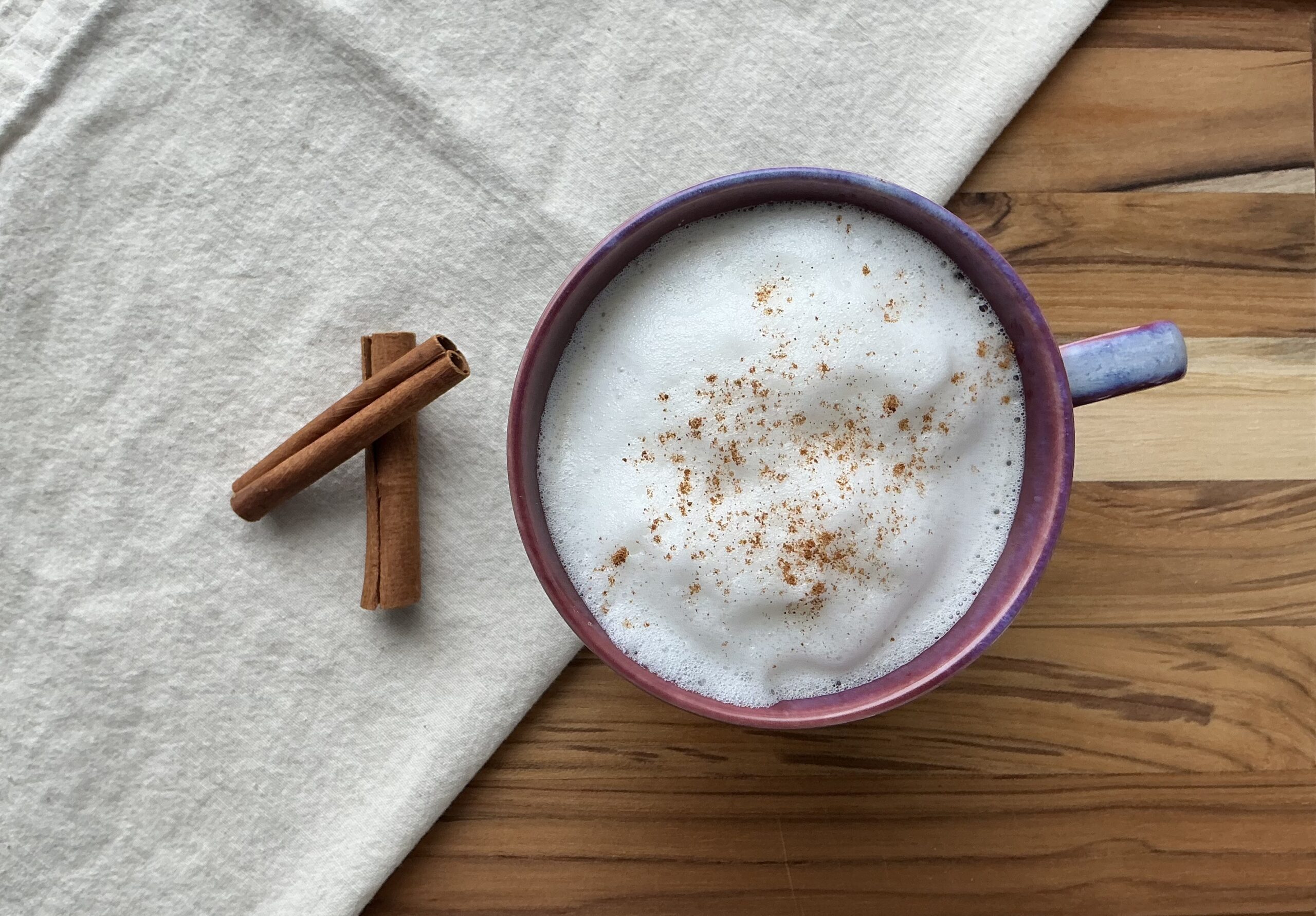 overhead shot of a foamy vanilla chai latte in a colorful mug with cinnamon sticks