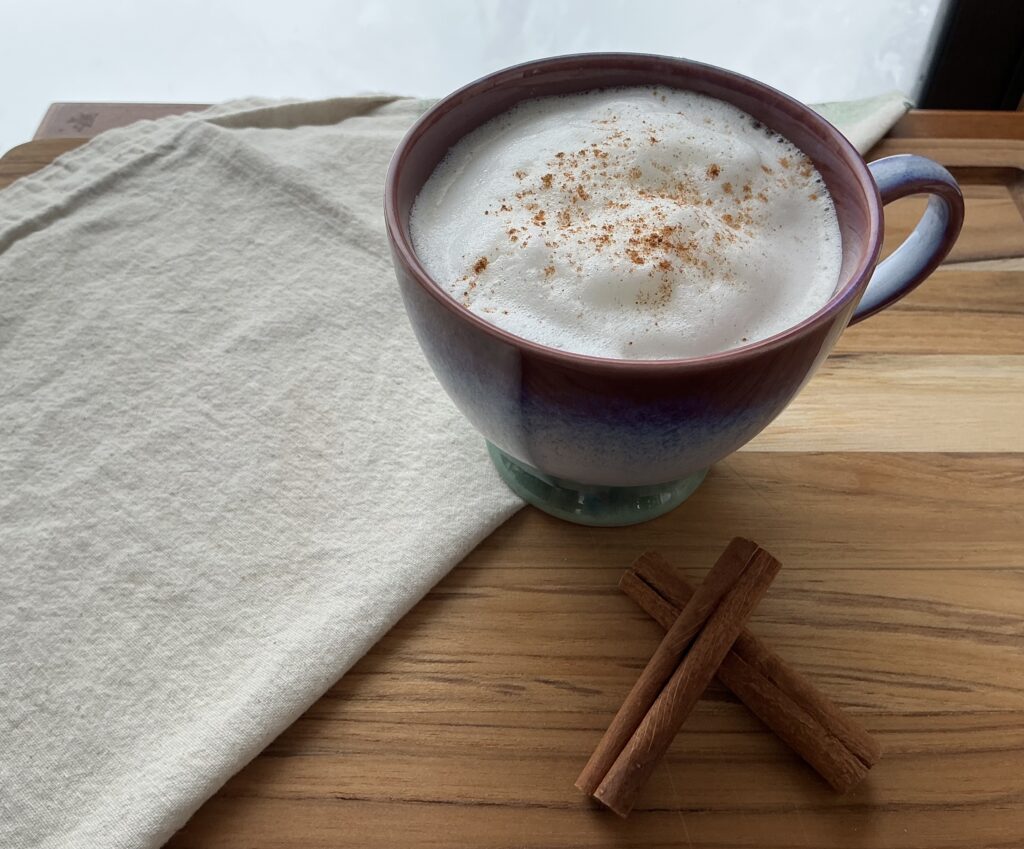 Foamy vanilla chai latte on a board with a tea towel and cinnamon sticks