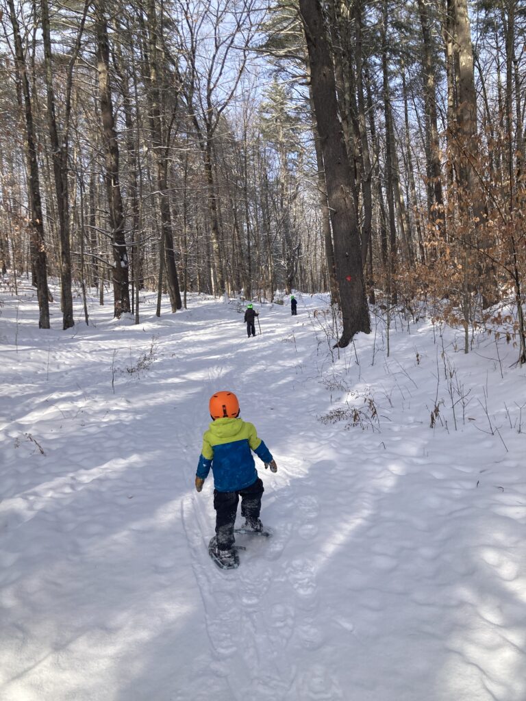 Small kid snowshoeing on a trail behind other kids 