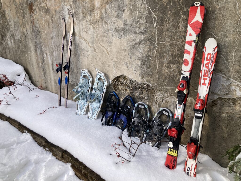 Skis and snowshoes leaning up against a wall. 